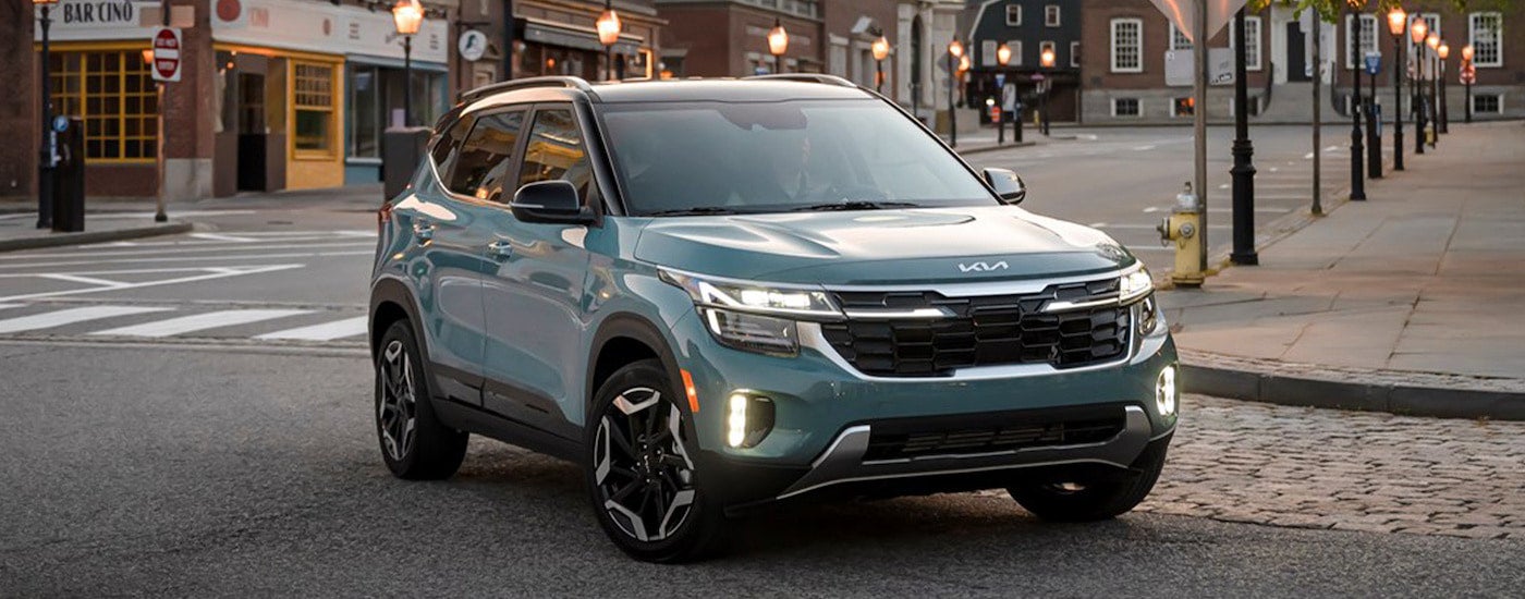 A teal Kia Seltos turing left on a city street lined with light posts