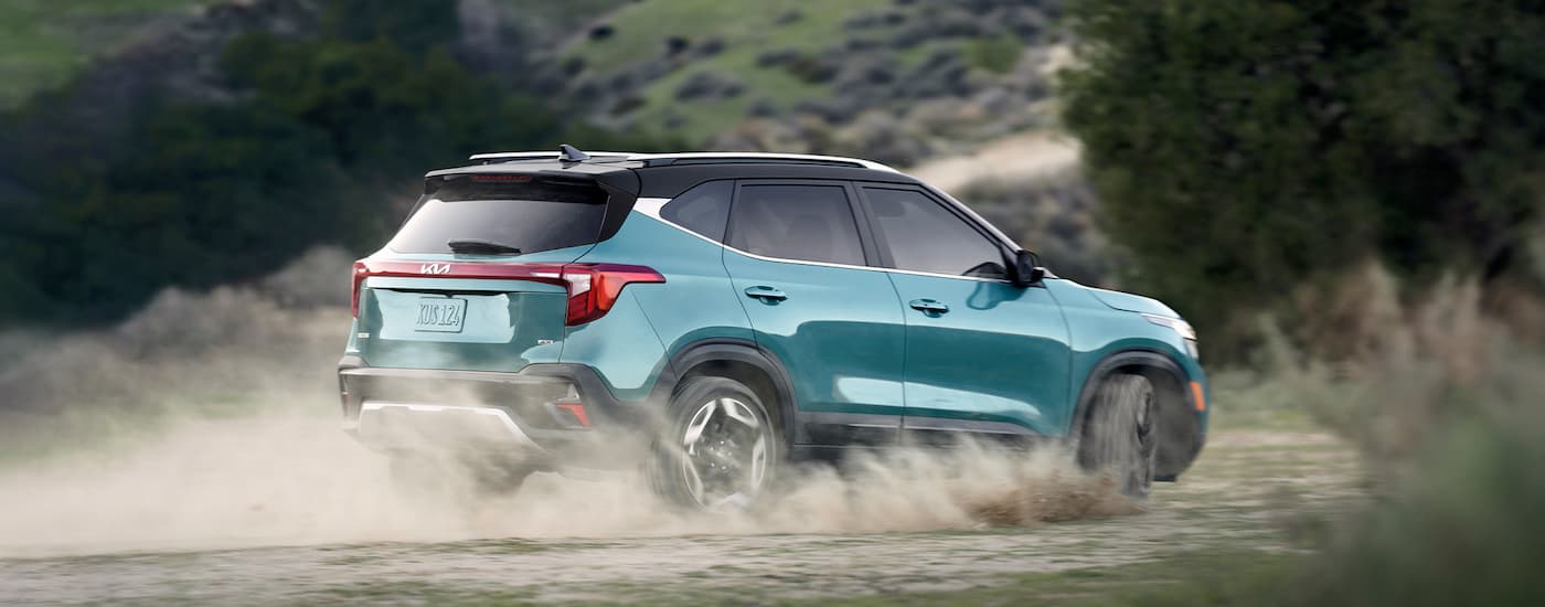 A teal Kia Seltos kicking up dust while driving in a dirt field